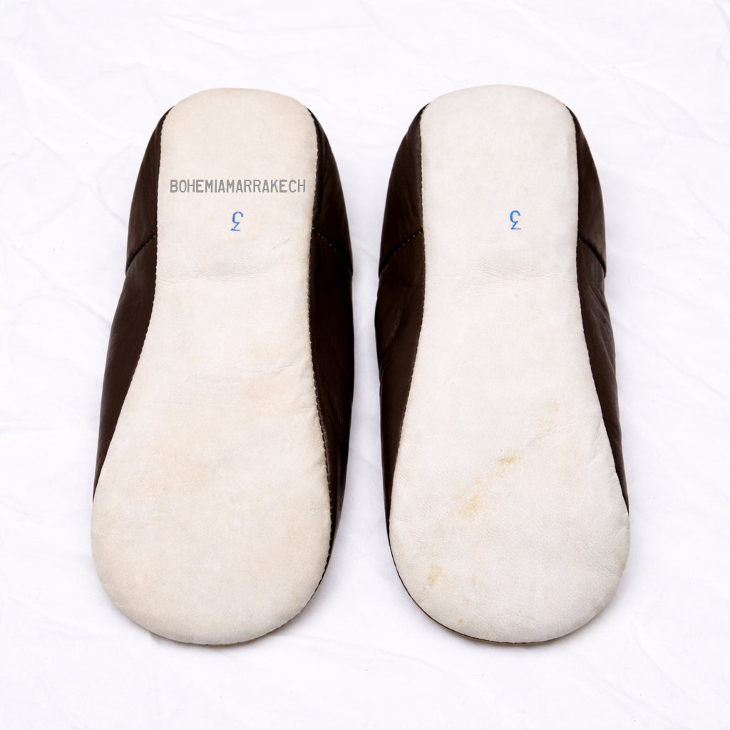Dark brown Moroccan leather babouche slippers with plain minimalist design on wooden floor