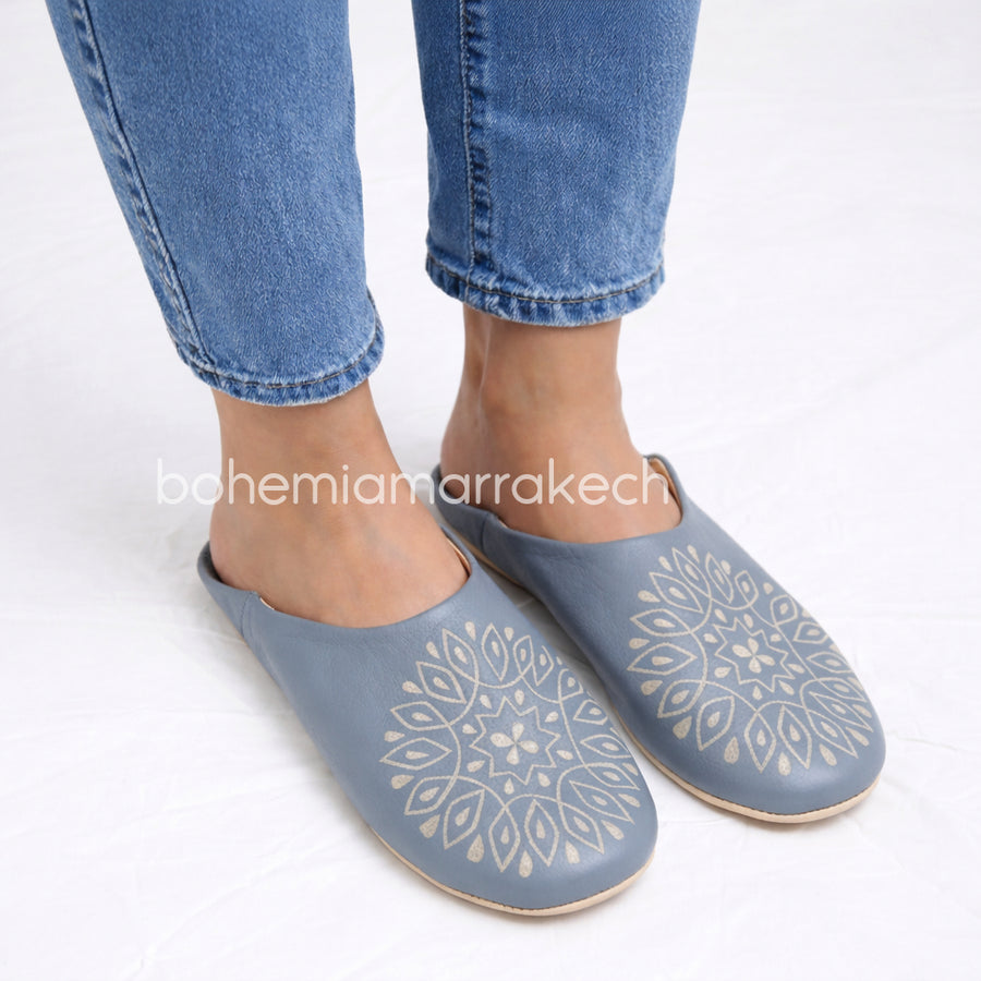 Handmade gray Moroccan babouche slippers with hand-carved geometric leather design on a light yellow background