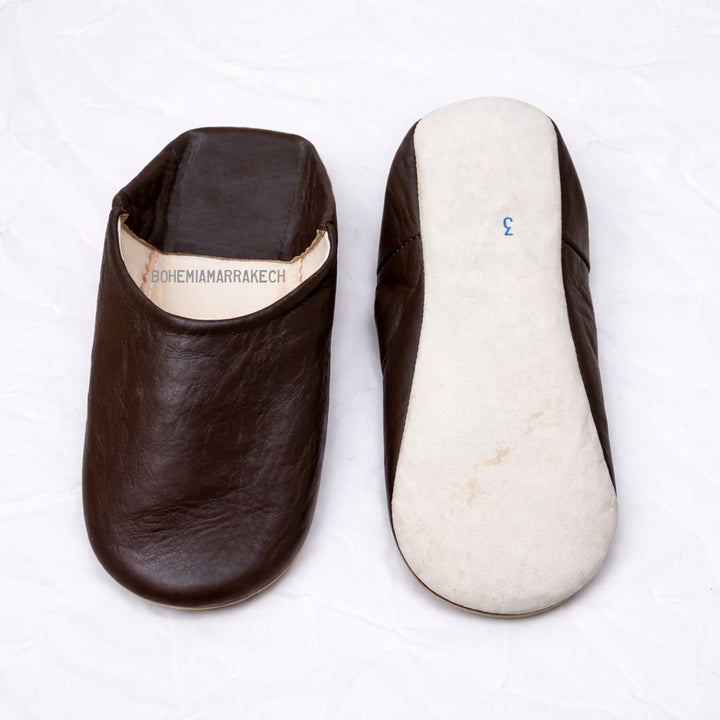 Dark brown Moroccan leather babouche slippers with plain minimalist design on wooden floor