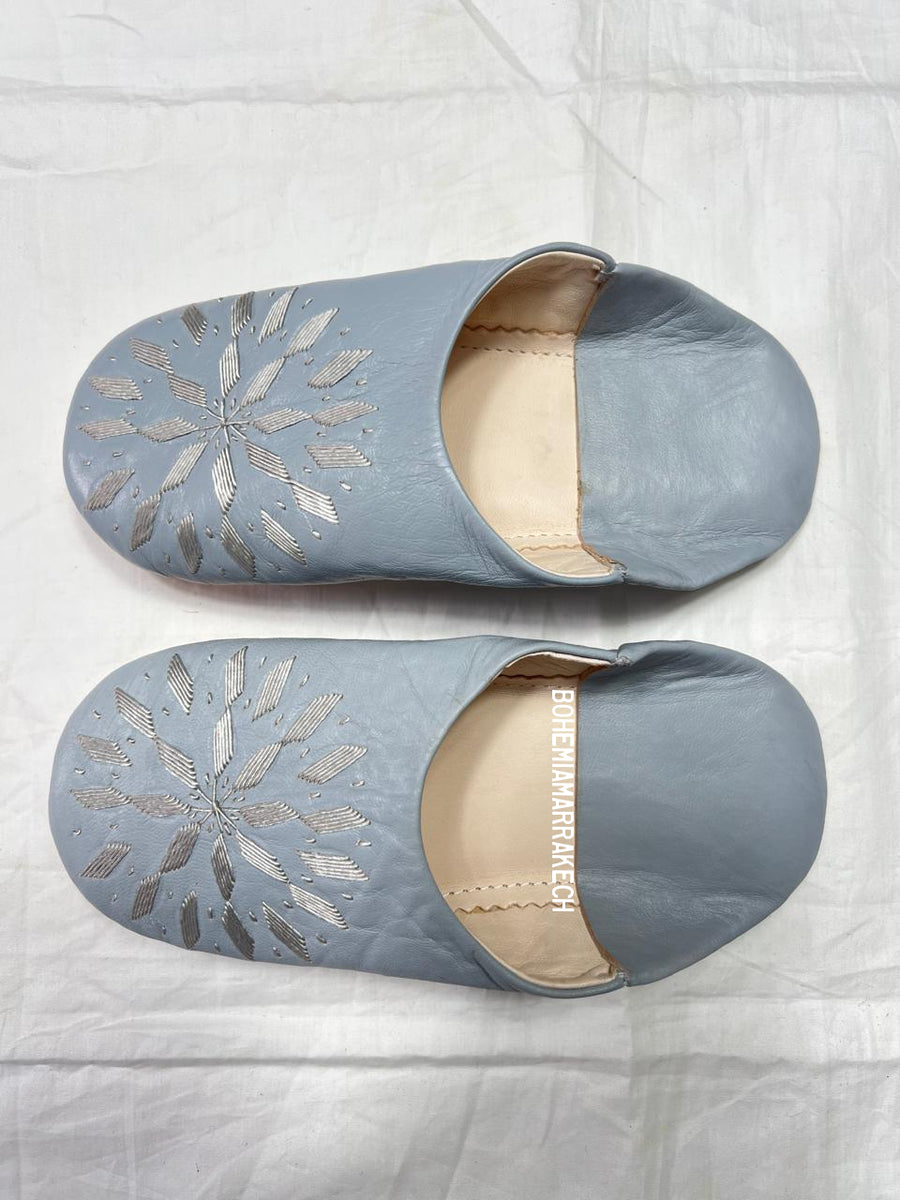 Light gray Moroccan babouche slippers with stitched geometric leather design on light yellow background