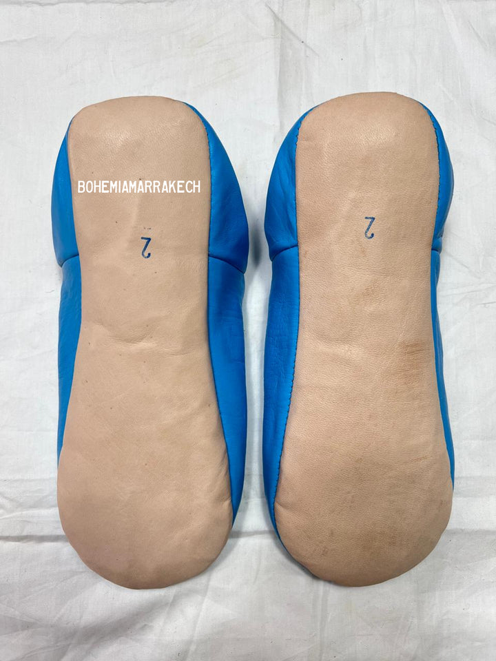 Blue Moroccan babouche slippers with stitched geometric leather design on white background