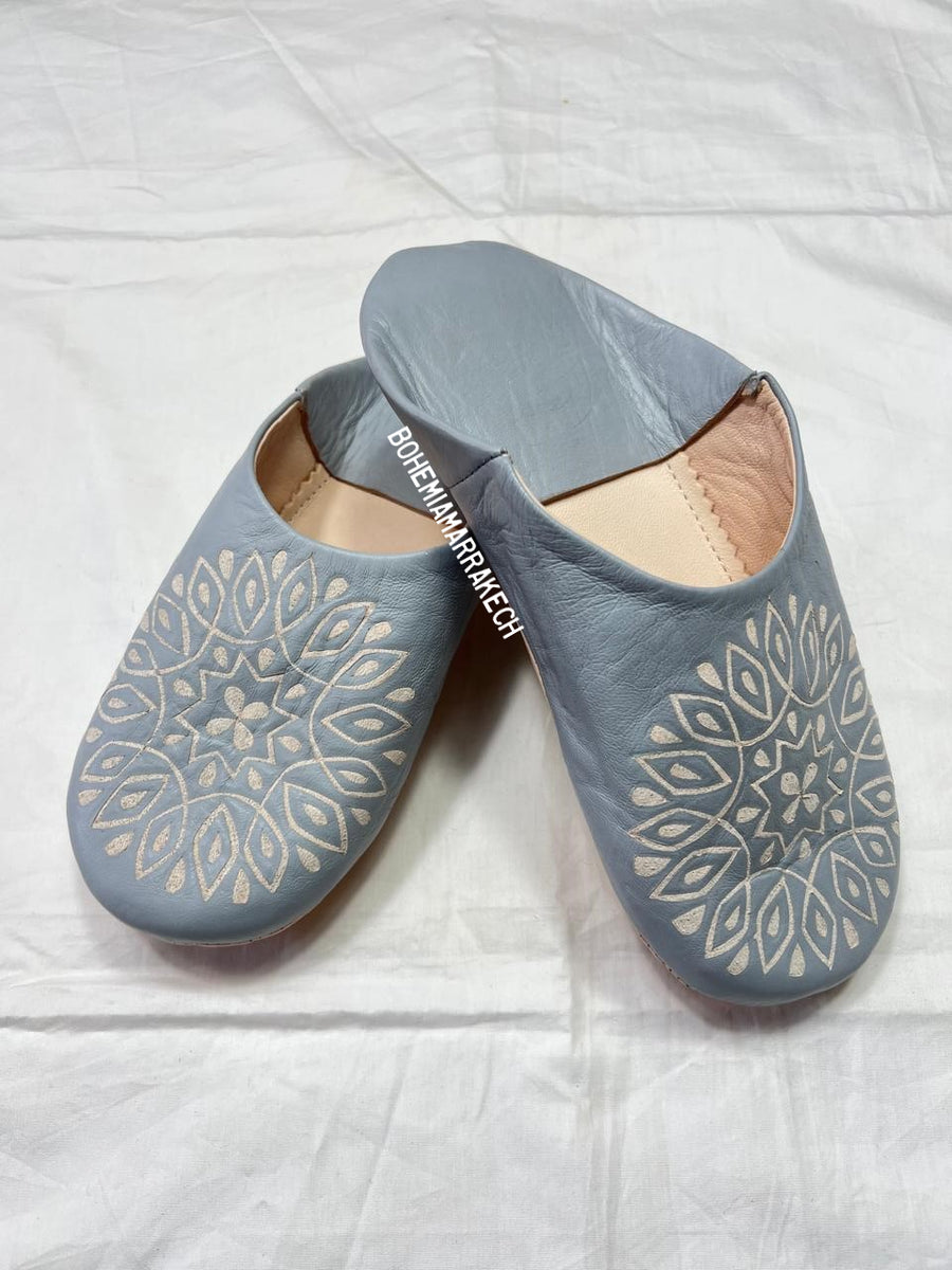 Handmade gray Moroccan babouche slippers with hand-carved geometric leather design on a light yellow background