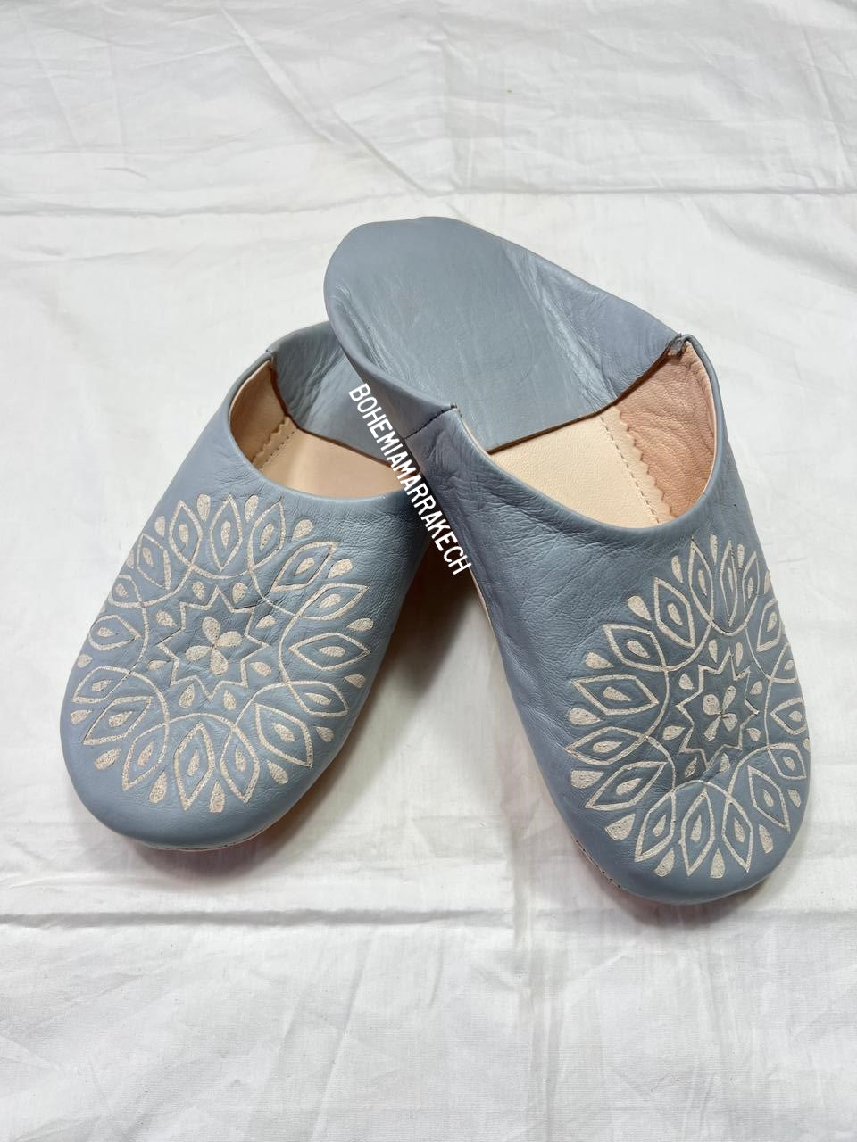 Handmade gray Moroccan babouche slippers with hand-carved geometric leather design on a light yellow background