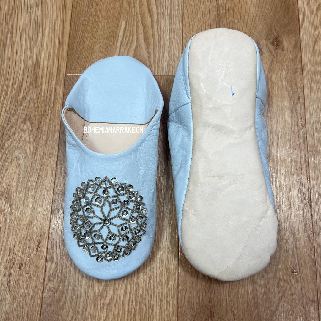 Light blue Moroccan babouche slippers handmade in leather with beaded geometric design, worn on model