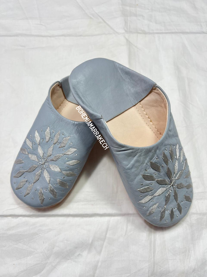 Light gray Moroccan babouche slippers with stitched geometric leather design on light yellow background