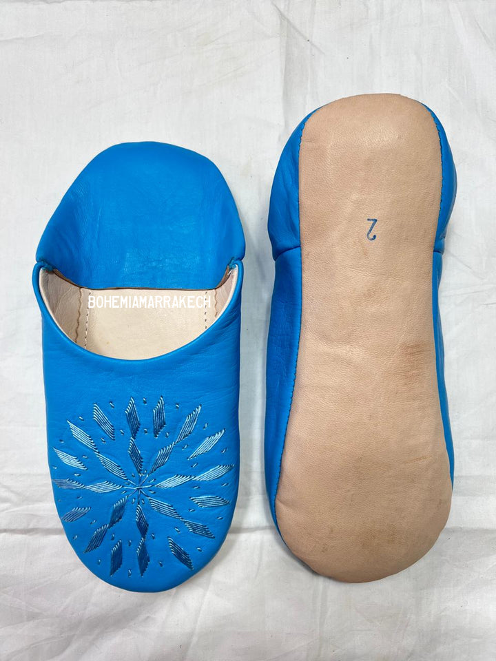 Blue Moroccan babouche slippers with stitched geometric leather design on white background