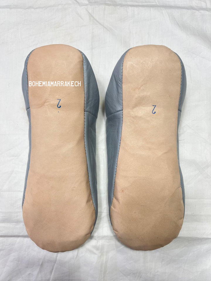 Handmade gray Moroccan babouche slippers with hand-carved geometric leather design on a light yellow background