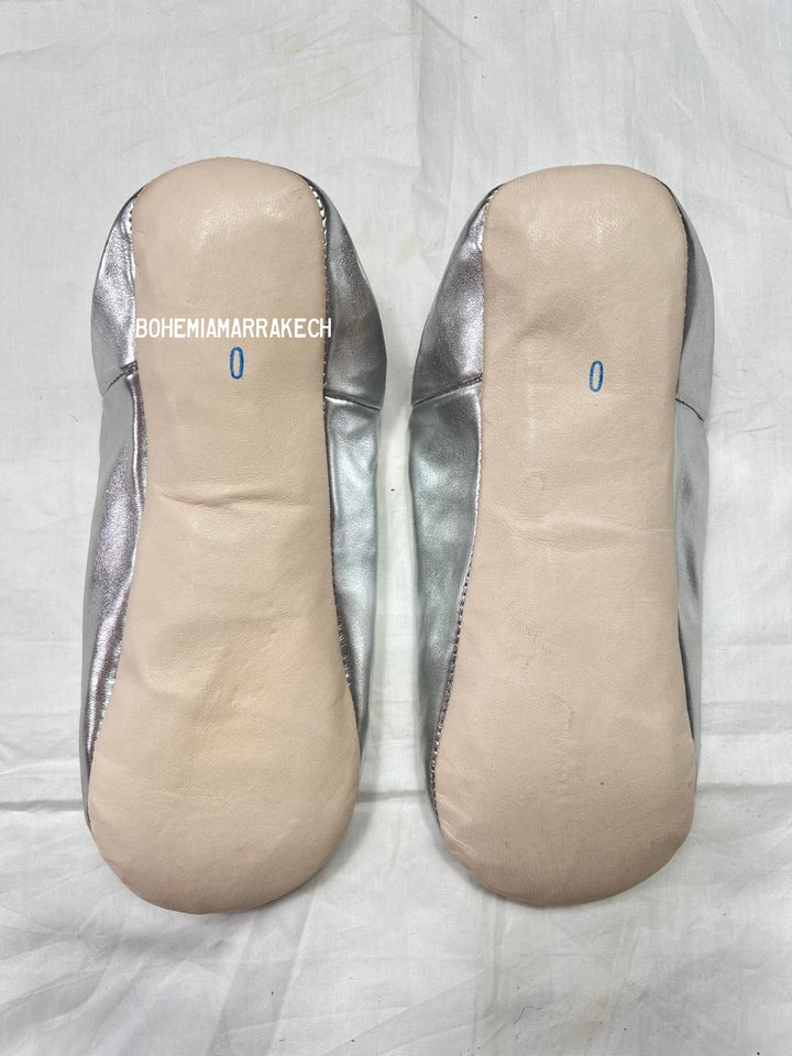 Silver Moroccan babouche slippers with tassel detail on light yellow background