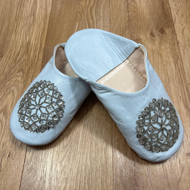 Light blue Moroccan babouche slippers handmade in leather with beaded geometric design, worn on model