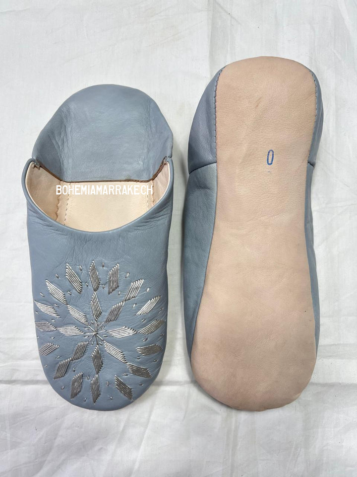 Light gray Moroccan babouche slippers with stitched geometric leather design on light yellow background