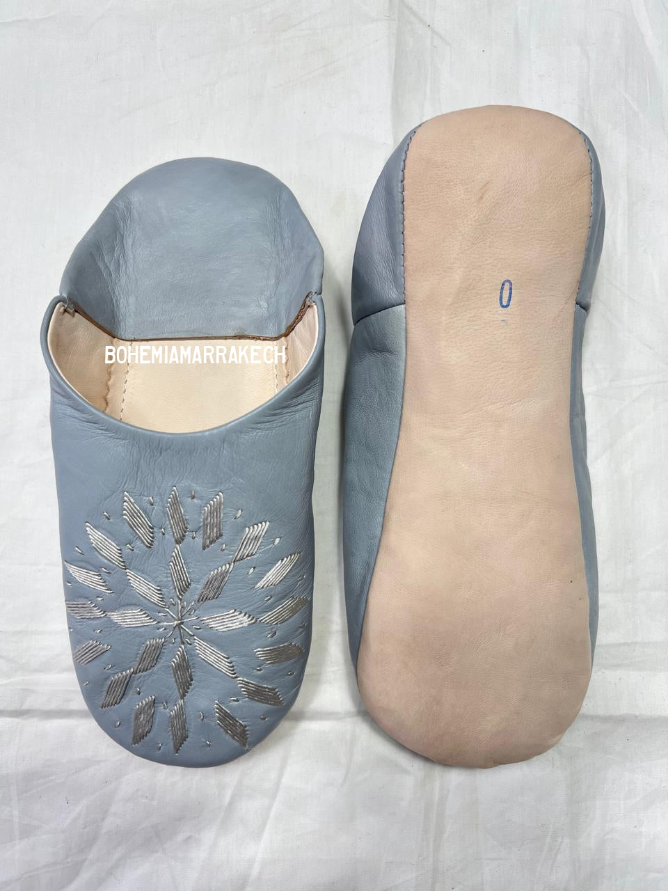 Light gray Moroccan babouche slippers with stitched geometric leather design on light yellow background