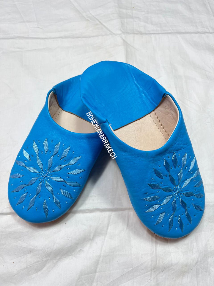 Blue Moroccan babouche slippers with stitched geometric leather design on white background