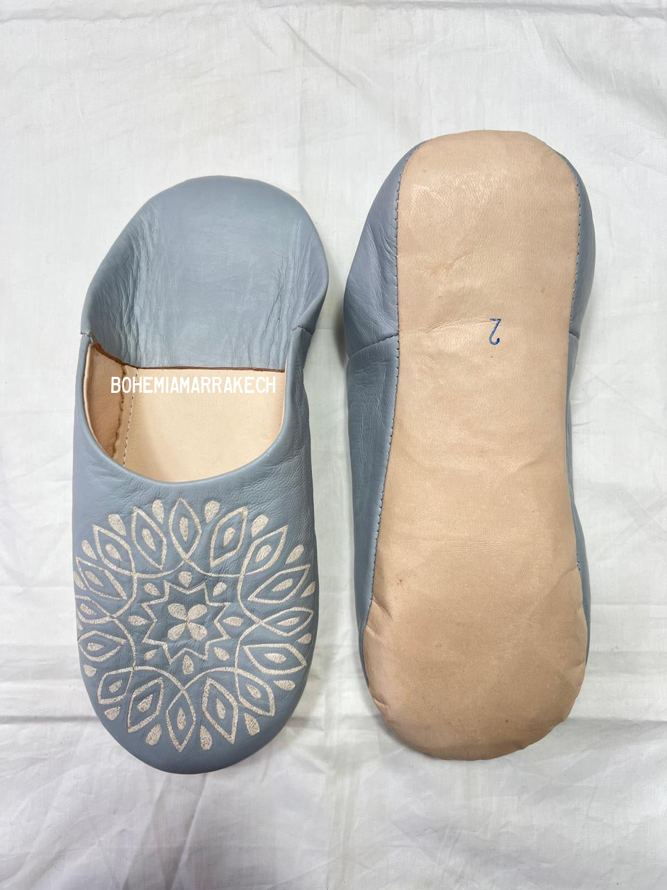 Handmade gray Moroccan babouche slippers with hand-carved geometric leather design on a light yellow background