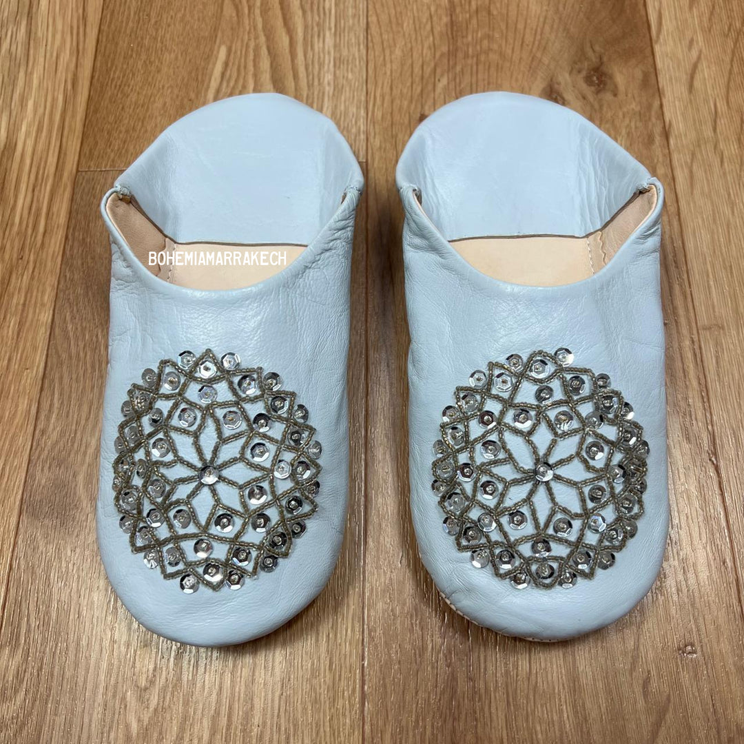 Light blue Moroccan babouche slippers handmade in leather with beaded geometric design, worn on model