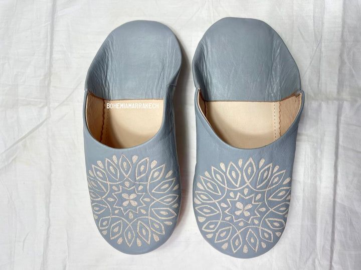 Handmade gray Moroccan babouche slippers with hand-carved geometric leather design on a light yellow background