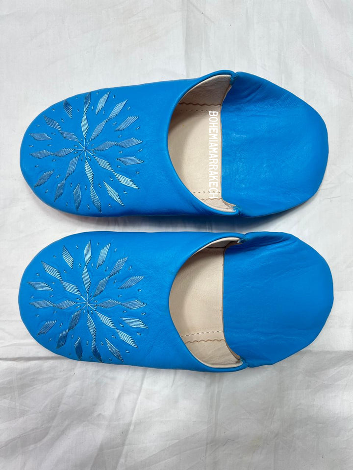 Blue Moroccan babouche slippers with stitched geometric leather design on white background