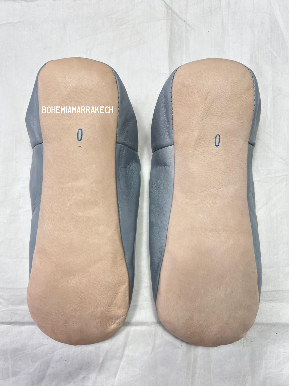 Light gray Moroccan babouche slippers with stitched geometric leather design on light yellow background