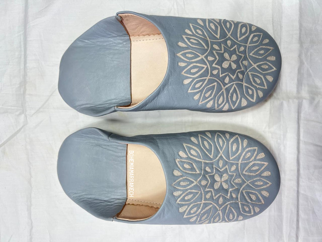 Handmade gray Moroccan babouche slippers with hand-carved geometric leather design on a light yellow background