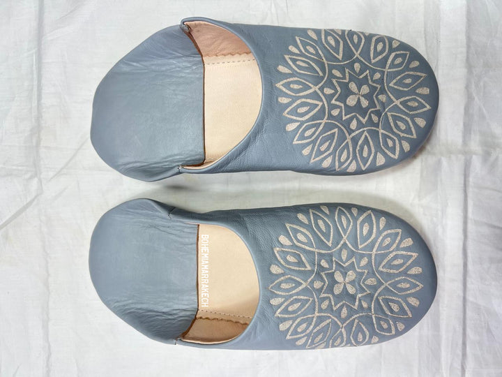 Handmade gray Moroccan babouche slippers with hand-carved geometric leather design on a light yellow background