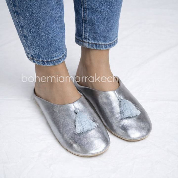 Silver Moroccan babouche slippers with tassel detail on light yellow background