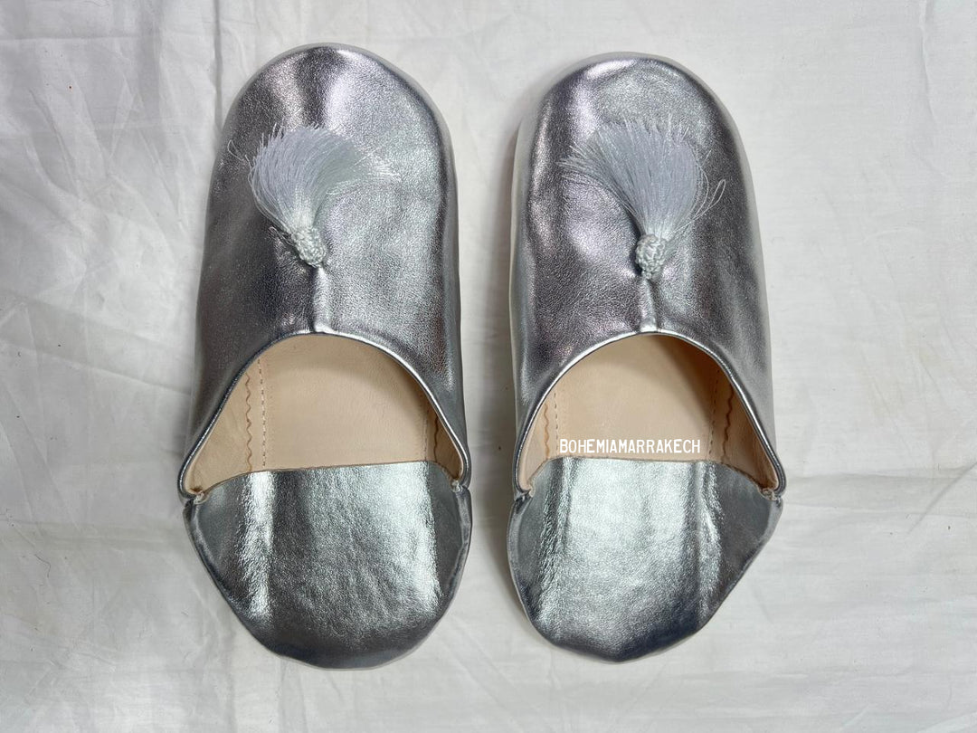 Silver Moroccan babouche slippers with tassel detail on light yellow background