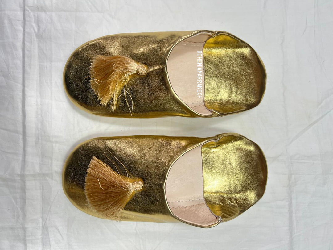 Gold Moroccan babouche slippers with tassel worn on model feet against white background