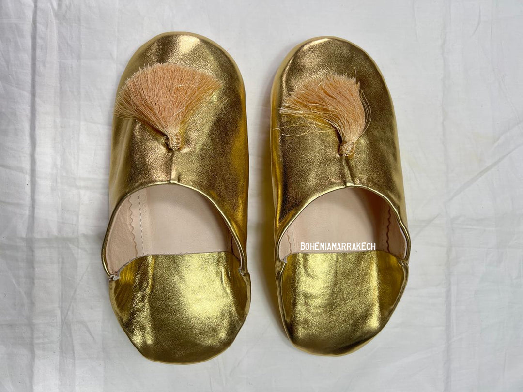 Gold Moroccan babouche slippers with tassel worn on model feet against white background