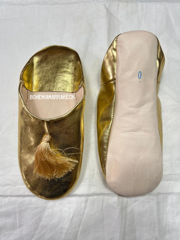 Gold Moroccan babouche slippers with tassel worn on model feet against white background