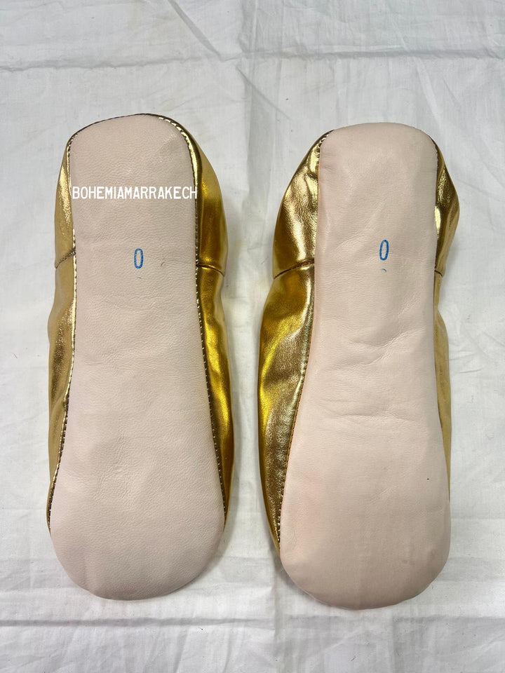 Gold Moroccan babouche slippers with tassel worn on model feet against white background