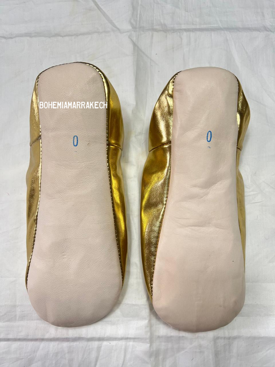 Gold Moroccan babouche slippers with tassel worn on model feet against white background