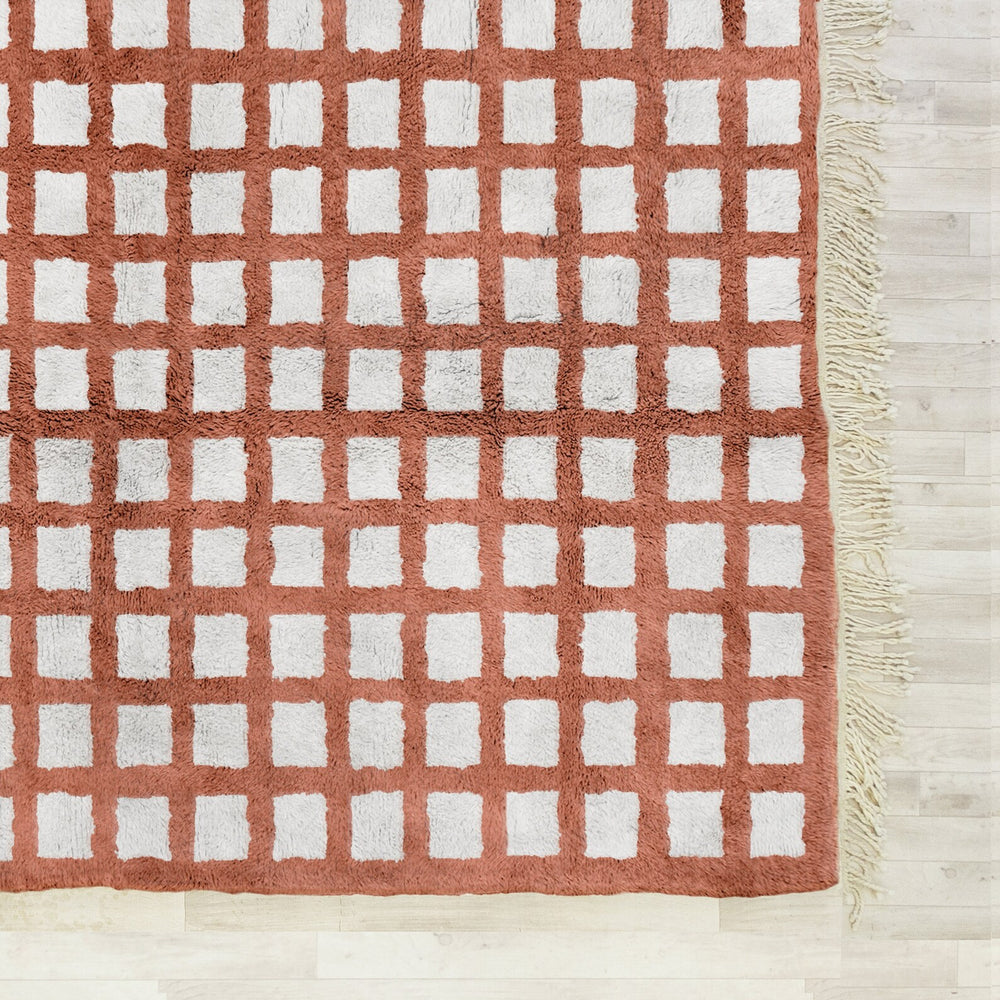 Rust-colored checkered rug with white squares on a light wooden floor.