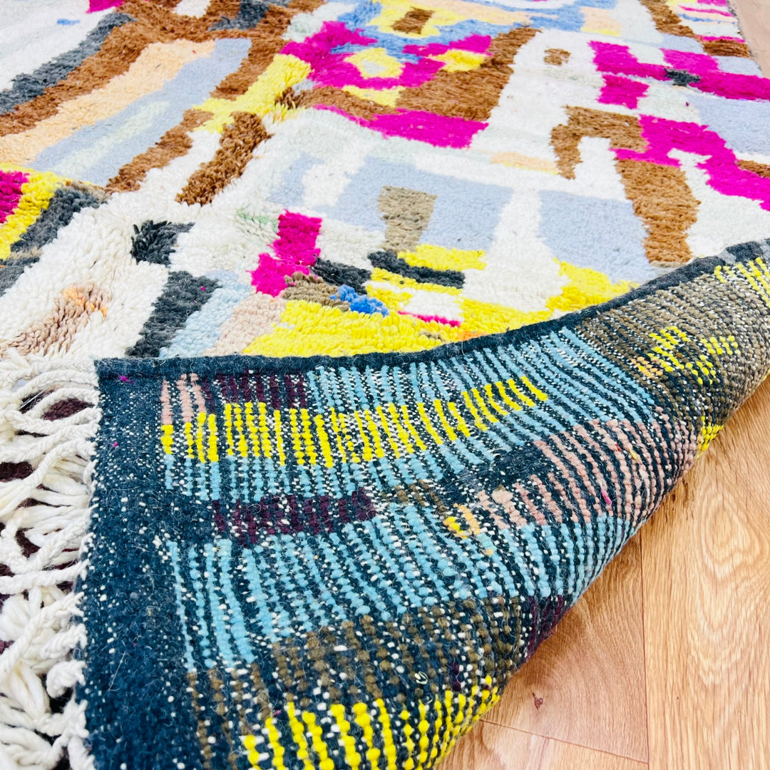 Colorful Moroccan wool rug with vibrant geometric patterns in magenta, mustard, blue, and brown hues, crafted by Berber artisans.