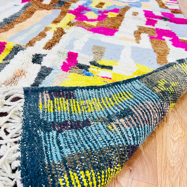 Colorful Moroccan wool rug with vibrant geometric patterns in magenta, mustard, blue, and brown hues, crafted by Berber artisans.