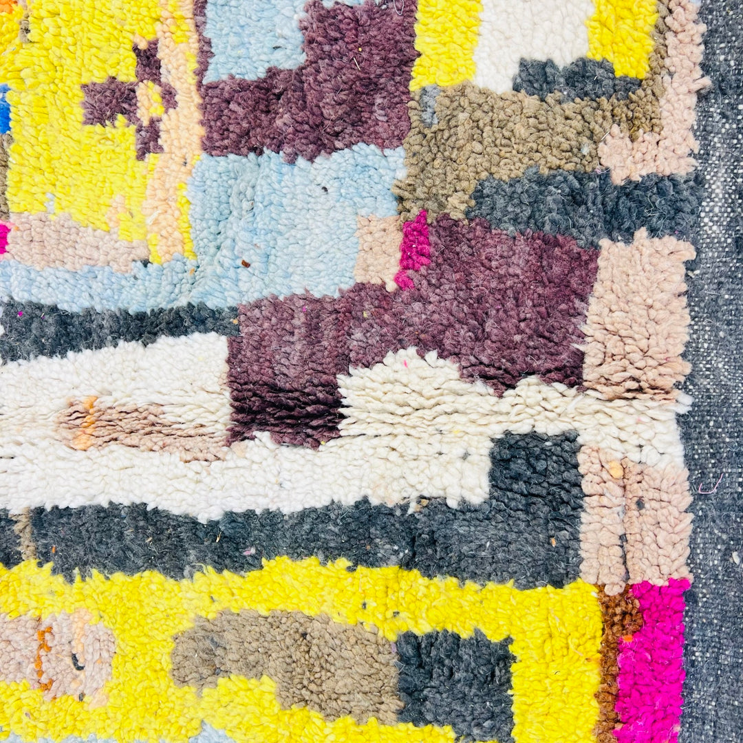 Colorful Moroccan wool rug with abstract geometric pattern in magenta, yellow, blue, and grey handmade by Berber artisans.