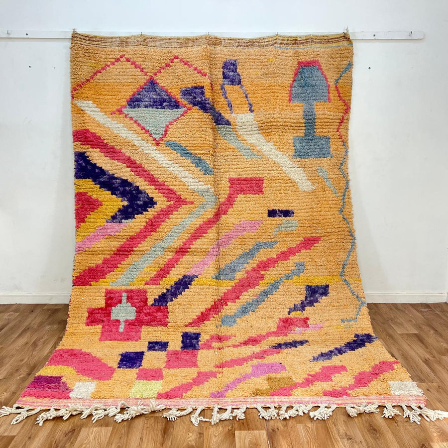 Vintage Moroccan wool rug with abstract geometric Berber design in warm ochre, pink, blue and green tones, handwoven in Morocco.